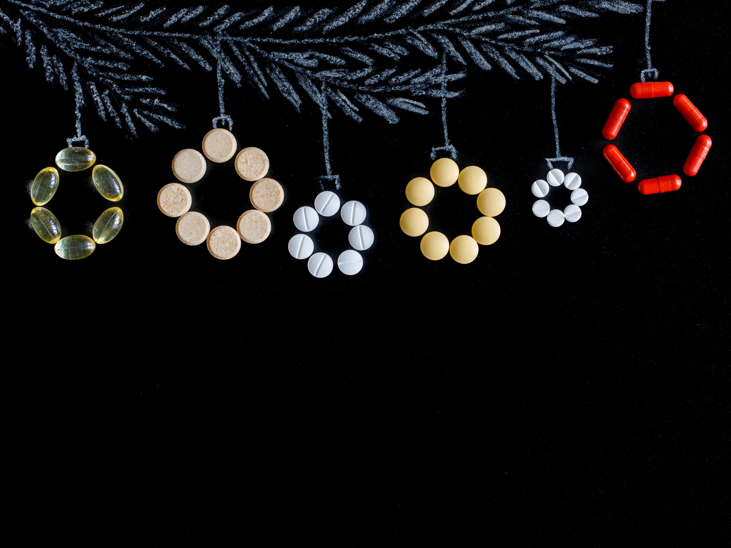 Symbolbild: Christbaumkugeln aus Tabletten und Kapseln geformt hängen an einem weißen Ast aus Kreide gezeichnet.