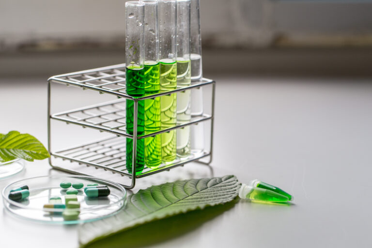 Symbolbild: Reagenzgläser mit verschieden grün gefärbten Flüssigkeiten. daneben liegen Blätter und Tabletten.