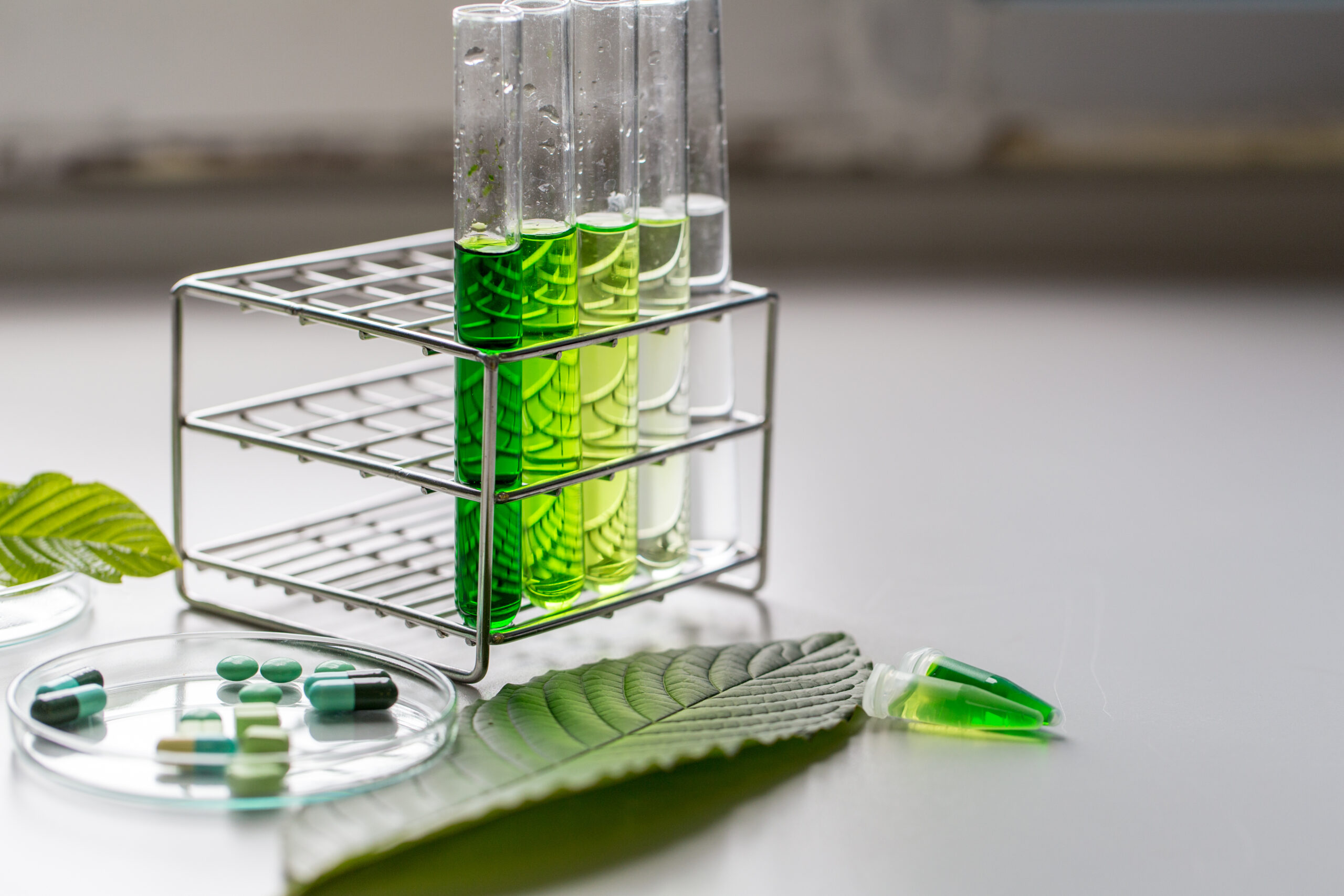 Symbolbild: Reagenzgläser mit verschieden grün gefärbten Flüssigkeiten. daneben liegen Blätter und Tabletten.