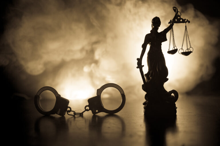 Symbolbild: Eine Statue von Justitia mit Handschellen vor Nebel.