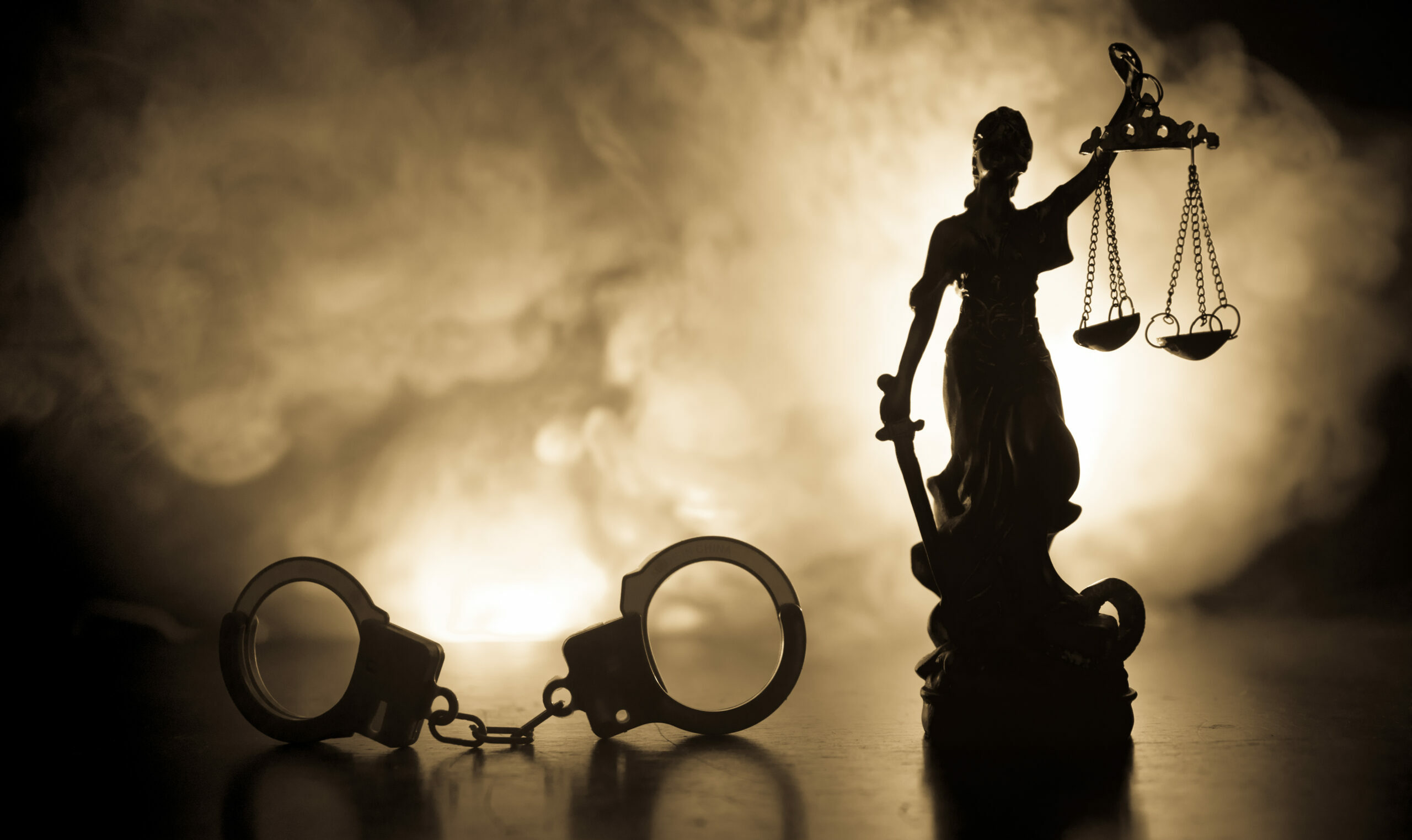 Symbolbild: Eine Statue von Justitia mit Handschellen vor Nebel.