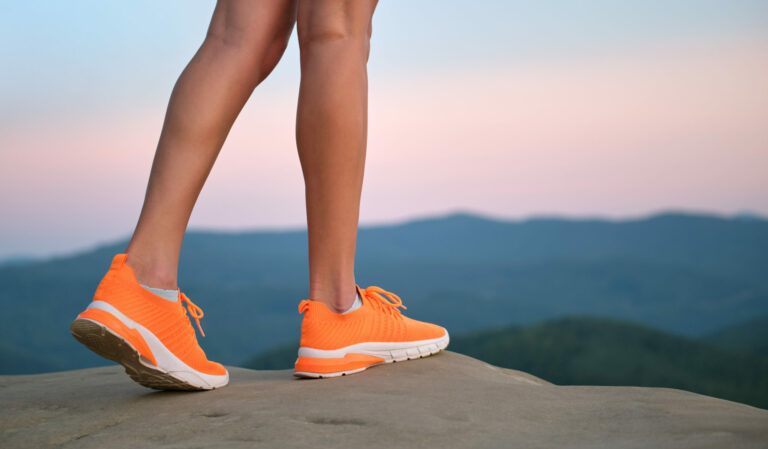 Symbolbild: Orange Senkers und Frauenbeine stehen auf einem Stein.