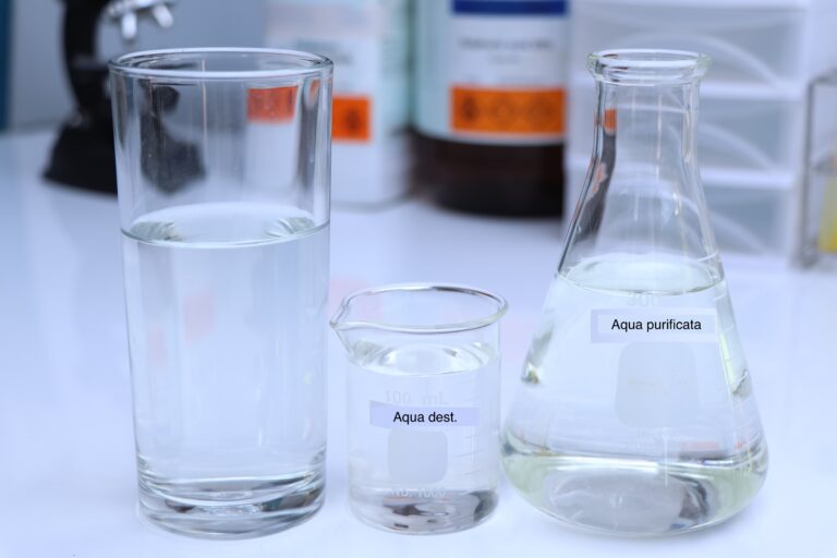 Symbolbild: Drei Glasgeräte im Labor mit Wasser gefüllt. Die Etiketten kennzeichnen es als Aqua Dest und Aqua Purificata.