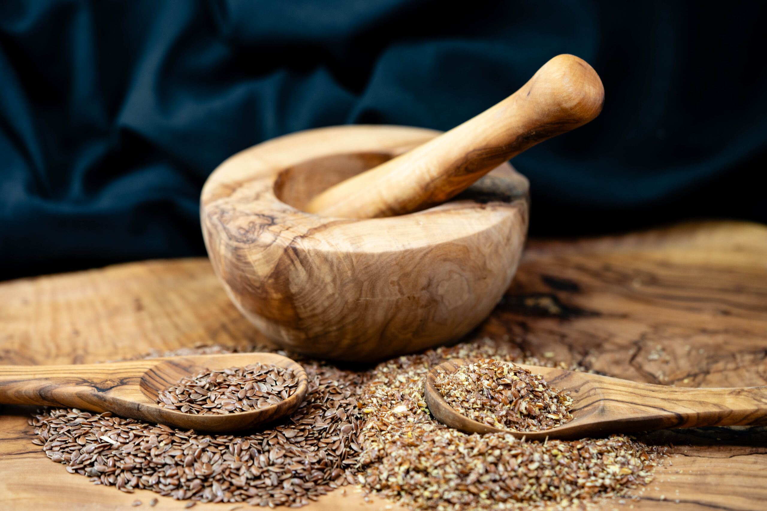 Symbolbild: Leinsamen geschrotet und ganz liegen neben einer Patene aus Holz.