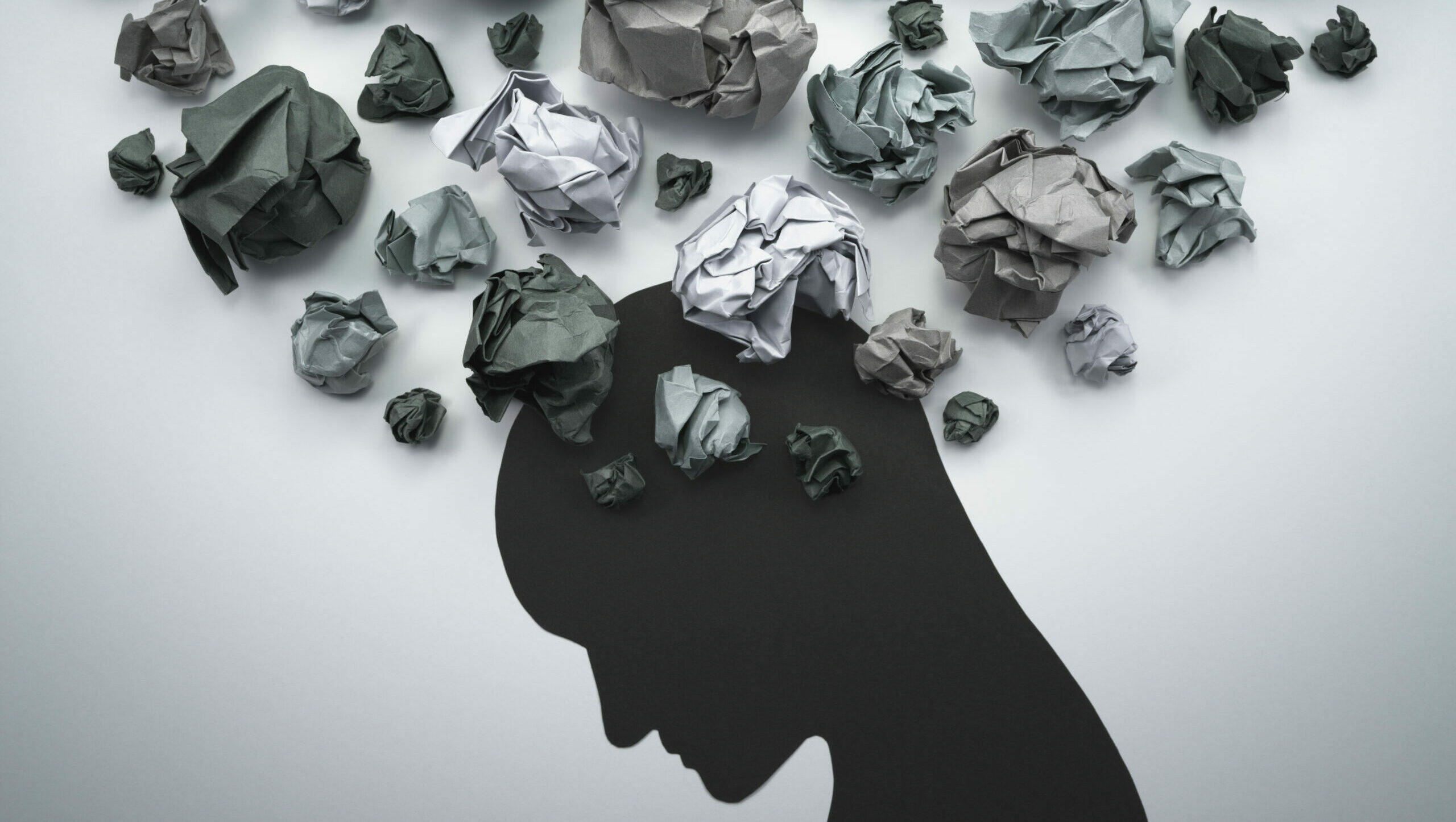 Symbolbild: Ein Kopf aus grauen Papier wird vom grauen Papierbällen umringt. Es deutet auf Angst hin.