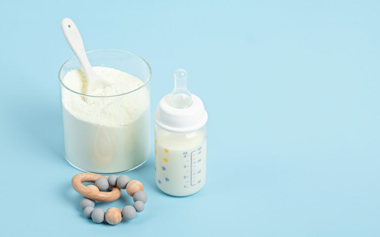 Symbolbild: Eine Babyflasche mit Rassel. Daneben steht ein Gefäß mit Milchpulver.