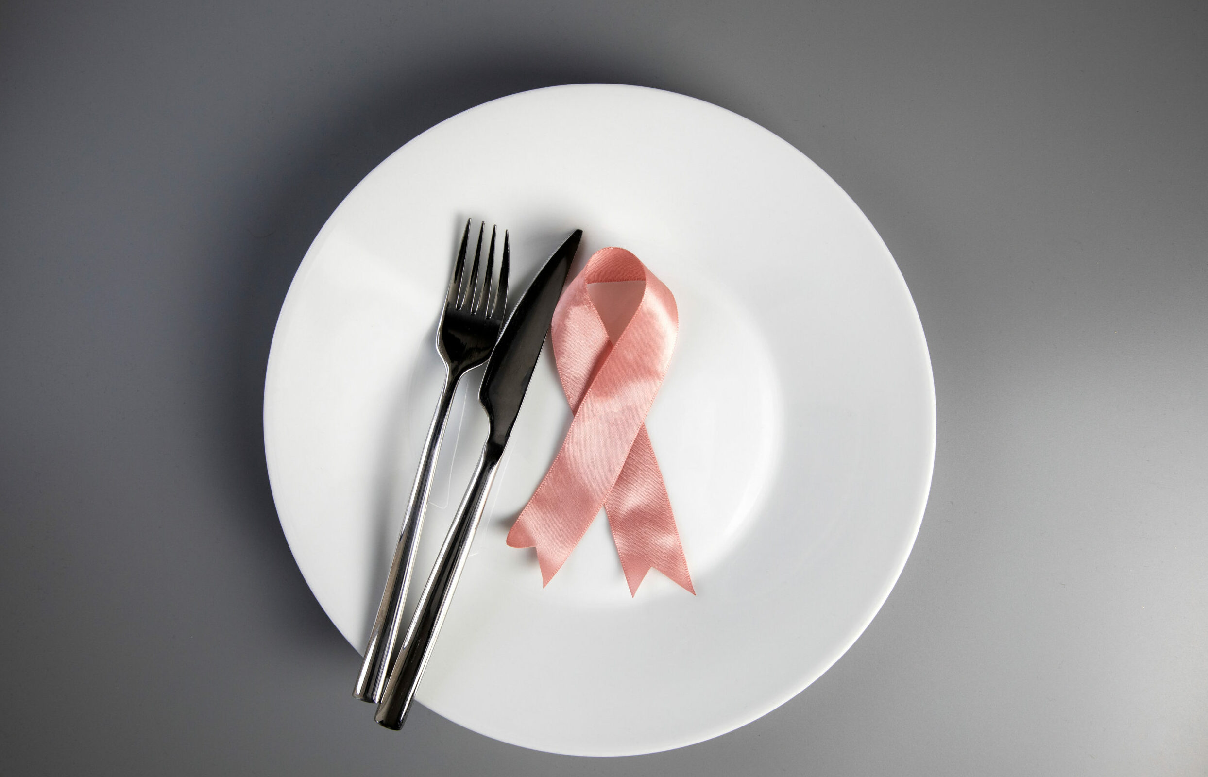 Symbolbild: Eine Pinke schleife liegt auf einem Teller. Daneben Messer und Gabel.