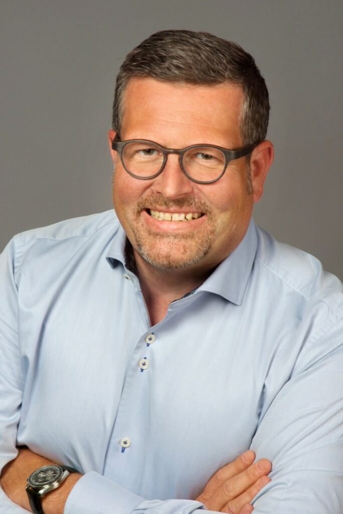 Franz Schätz überkreuzt die Armre und lächelt in die Kamera.