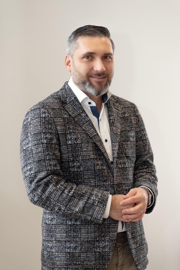 Harald Markut steht in einem grauen Anzug und faltet seine Hände. Er Lächelt