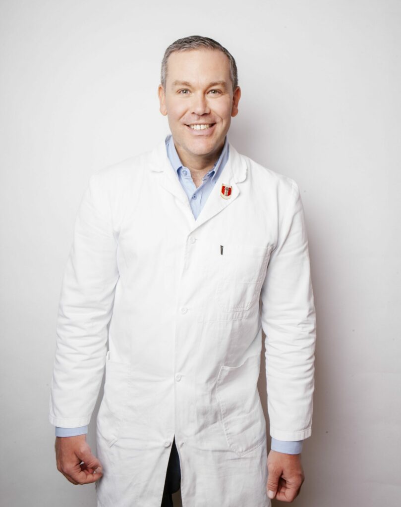 Apotheker Thomas Müller Uri in seinem weißen Mantel. Er lächelt.