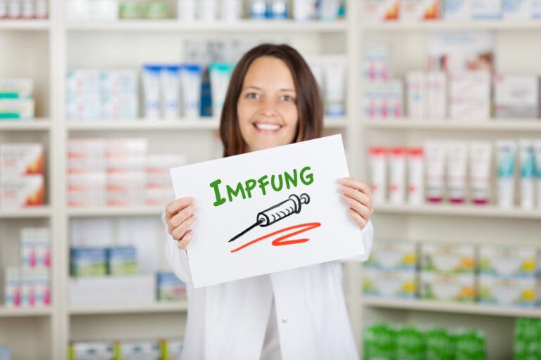 Symbolbild: Eine lächelnde Apothekerin hält ein Schild mit "Impfung" in der Hand.