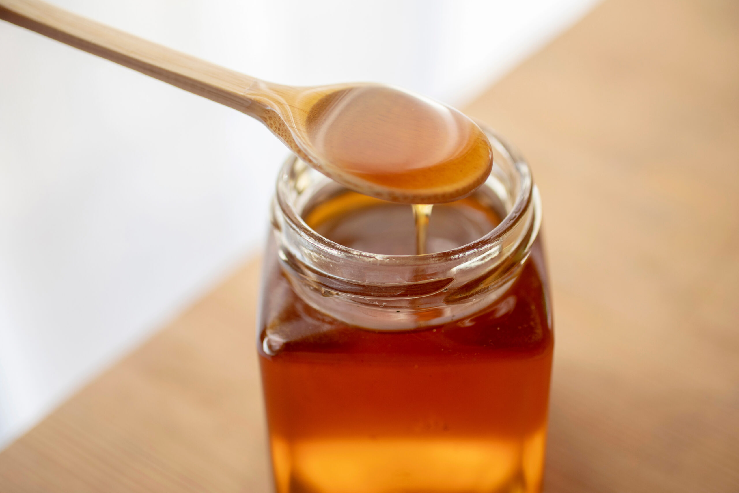Symbolbild: Ein Glas Honig mit einem Löffel darin. Der Honig tropft vom Löffel.