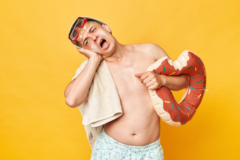 Symbolbild: Ein junger Mann hält sich das Ohr vor Schmerz. Er trägt einen Schwimmreifen und ein Handtuch.