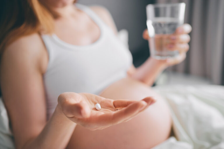 Symbolbild: Eine junge schwangere Frau mit Tablette und Wasserglas in der Hand.