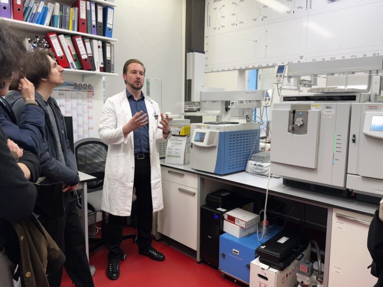Stefan Brenner steht vor seiner HPLC Anlage und erklärt der Gruppe etwas.
