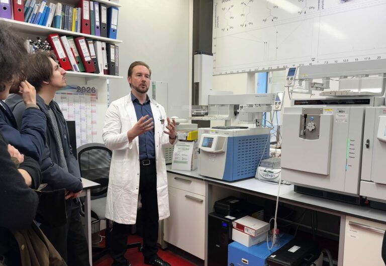 Stefan Brenner steht vor seiner HPLC Anlage und erklärt der Gruppe etwas.