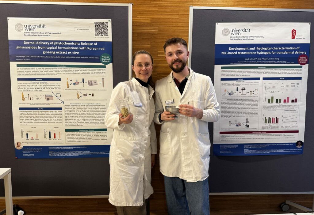 Die beiden Doktoranden stehen vor ihren Plakaten. Sie tragen weiße Mäntel.