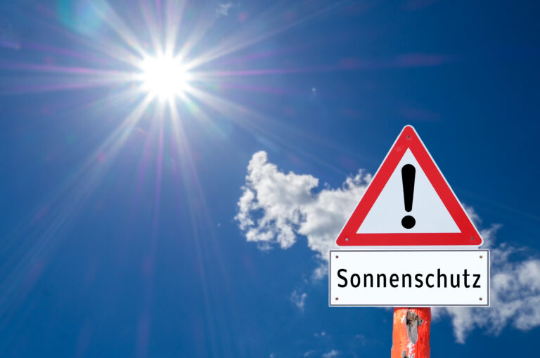 Symbolbild: Ein Warnschild mit der Aufschrift "Sonnenschutz" vor strahlendem Himmel.