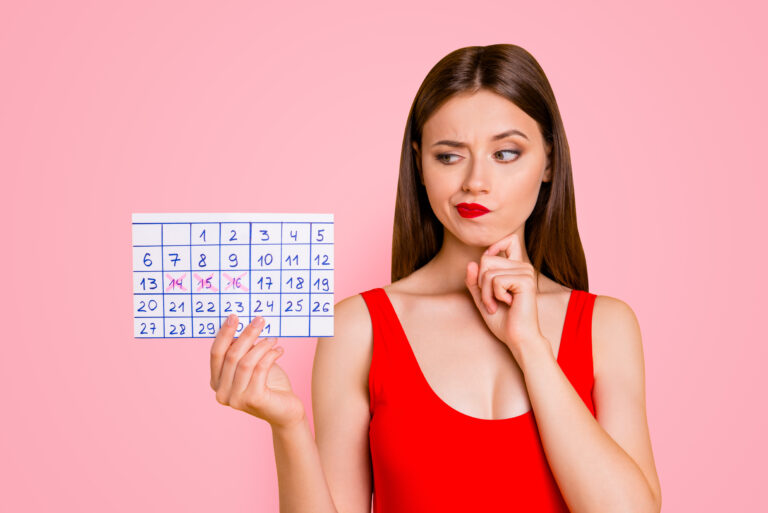 Symbolbild: Junge Frau im roten Badeanzug schaut auf einen Kalender mit drei roten kreuzen.