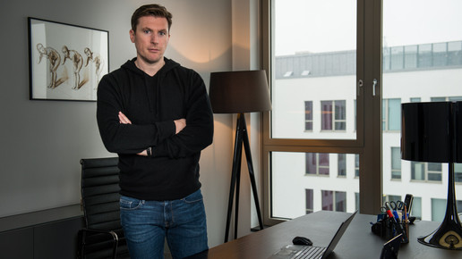 Dr.Fischer steht in einem Büro und hat die Arme verschränkt.