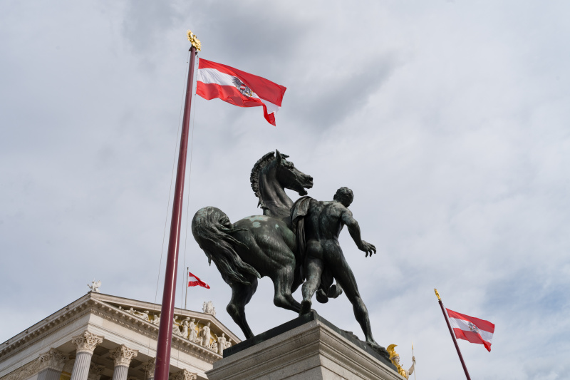 Symbolbild: Das Parlament in Wien. Man sieht eine Statue und die Österreichische Flagge.