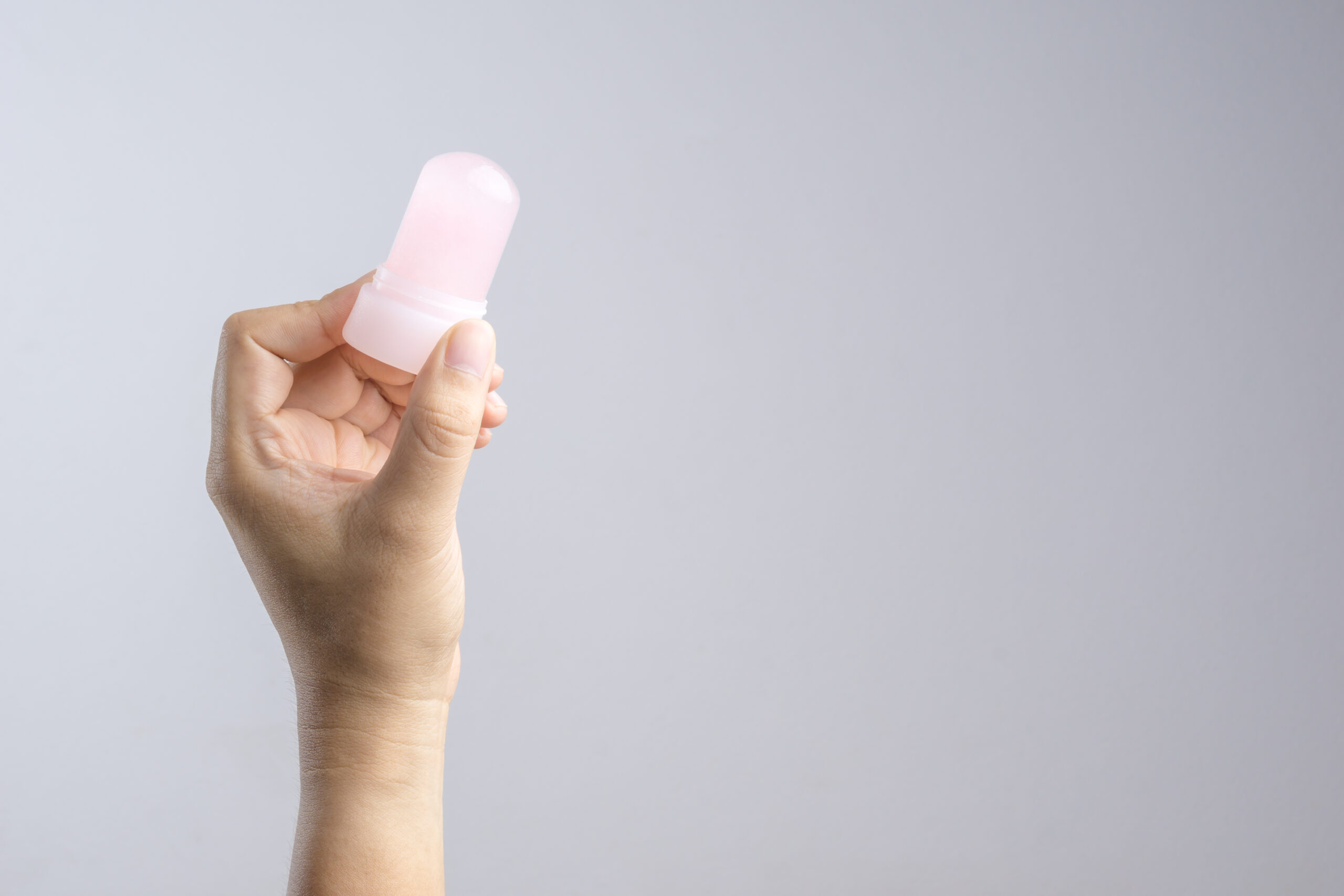 Symbolbild: Hand, die einen natürlichen Mineral-Alaun-Kristall-Stift hält und diesen als Unterarm-Deodorant auf weißem Hintergrund verwendet.