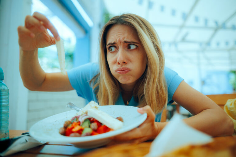 Symbolbild: Eine Frau hält ein Essen in die Höhe und begutachtet es skeptisch.