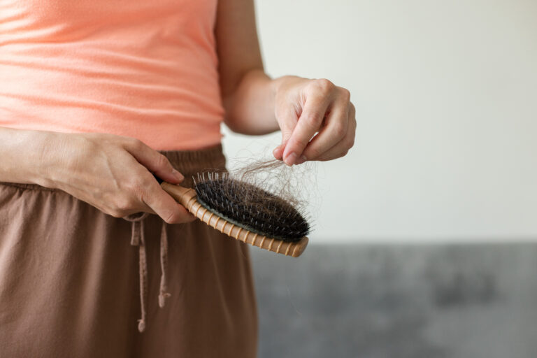 Symbolbild: Eine Frau haltet ihre Haarbürste und entfernt die Haare daraus.