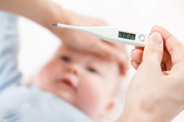 Symbolbild: Ein Fieberthermometer in einer Hand und die andere Hand liegt auf der Stirn des Babys auf.