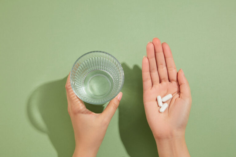 Symbolbild: Ein Glas in der einen Hand und Tabletten in der anderen Hand.