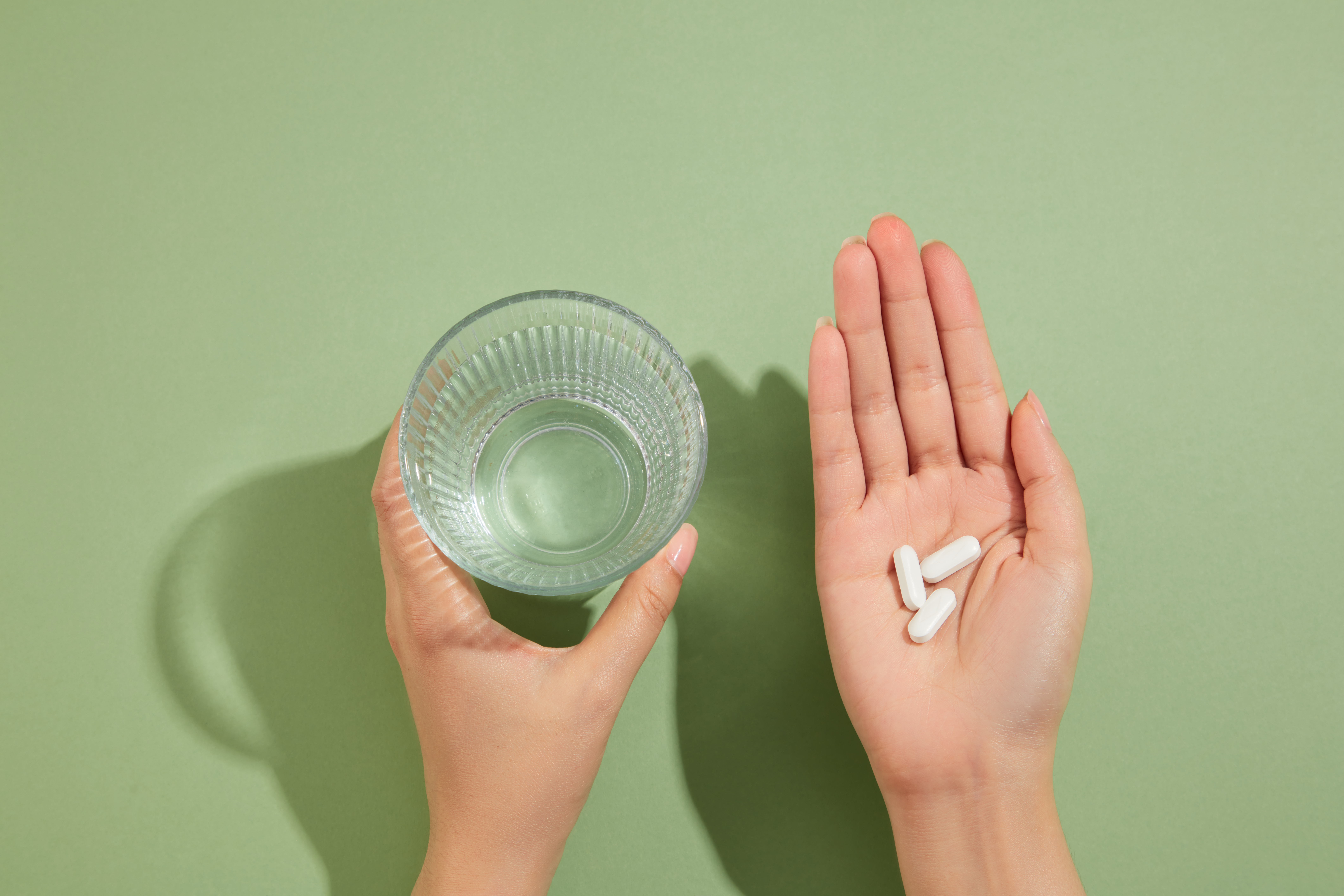 Symbolbild: Ein Glas in der einen Hand und Tabletten in der anderen Hand.