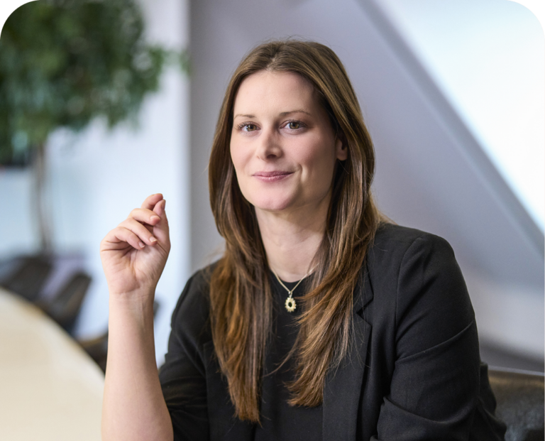 Martina Egger sitzt an einem Tisch. Sie trägt eine schwarze Bluse und lächelt.
