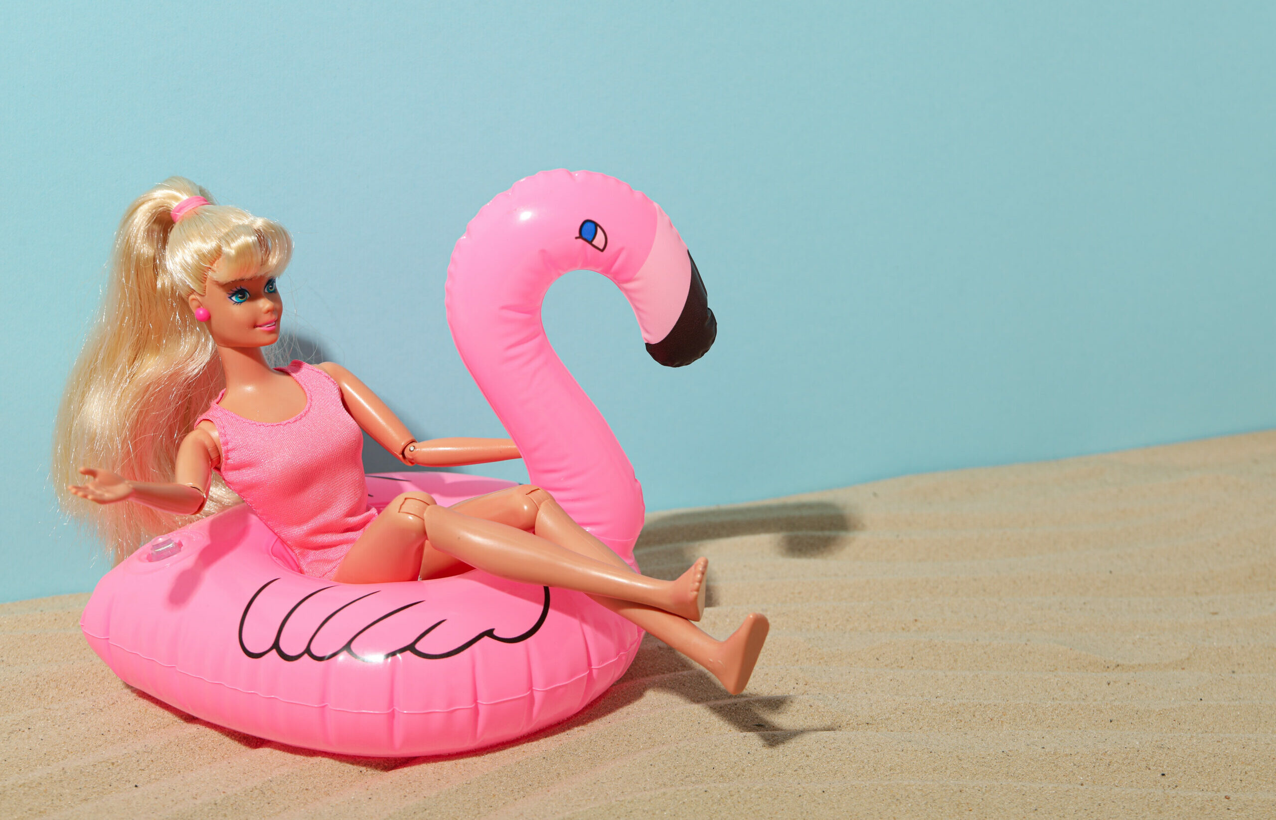 Symbolbild: Eine Barbie sitz auf einem Pinken Flamingo im Sand.