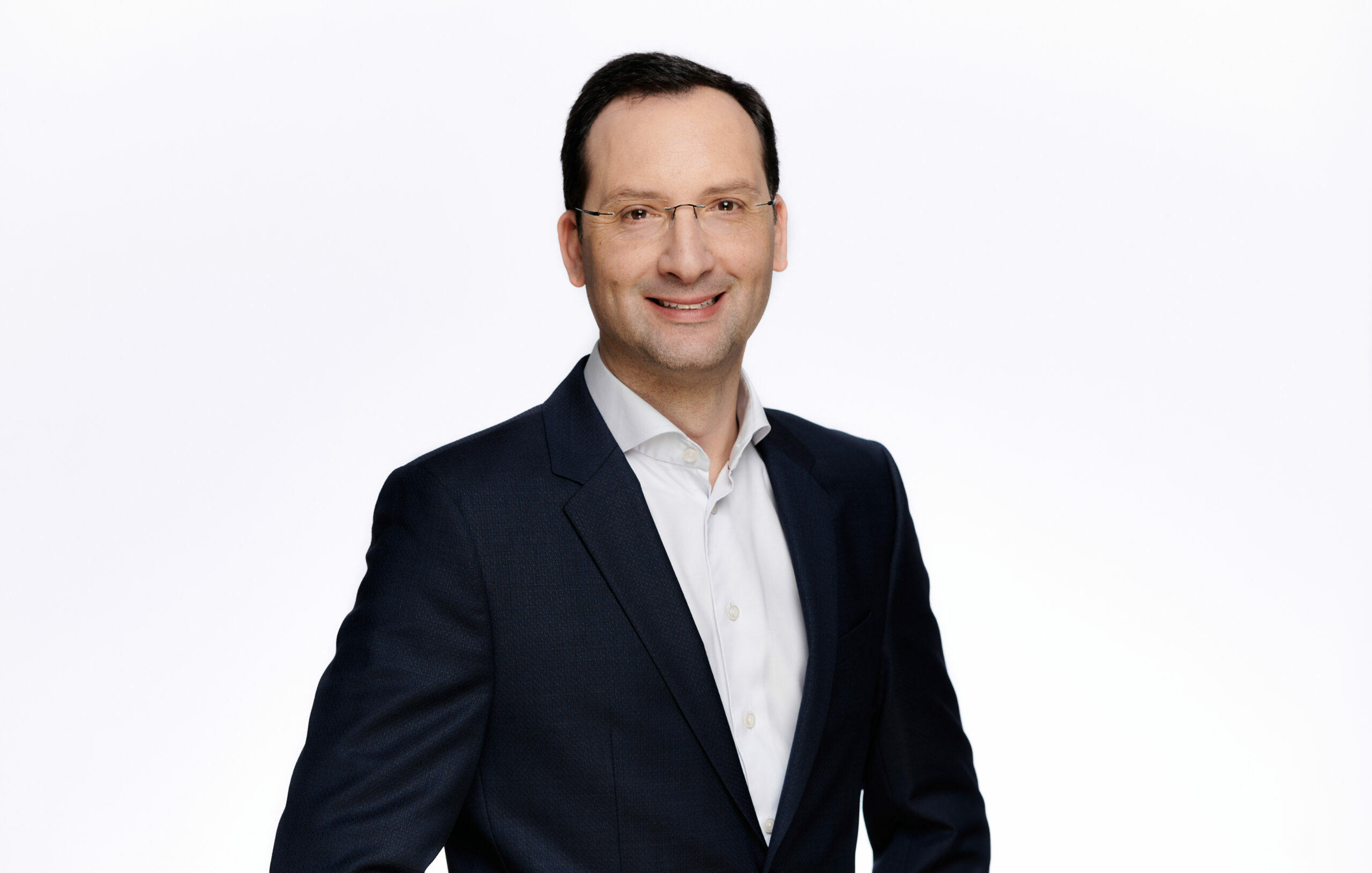 Julien Auger-Ottavi als Country President. Er trägt einen schwarzen Anzug und lächelt.