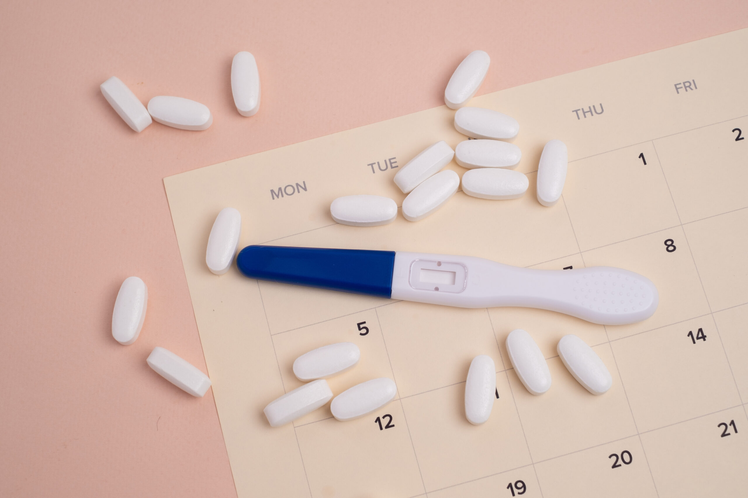 Symbolbild: Ein Schwangerschaftstest liegt auf einem Kalender neben vielen weißen Tabletten.